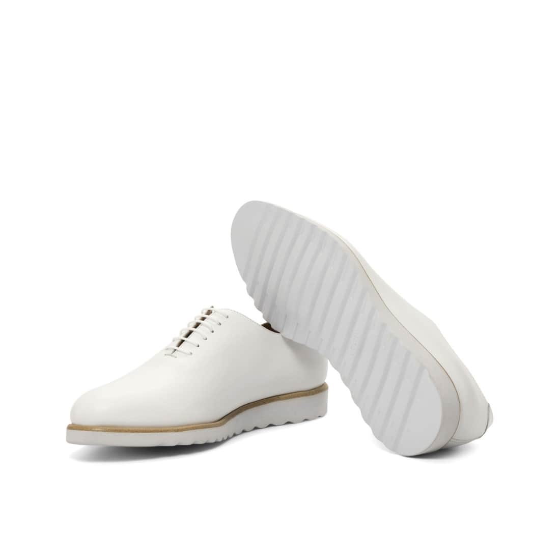 One Cut en cuir blanc, l’un couché qui montre sa semelle compensée blanche et striée