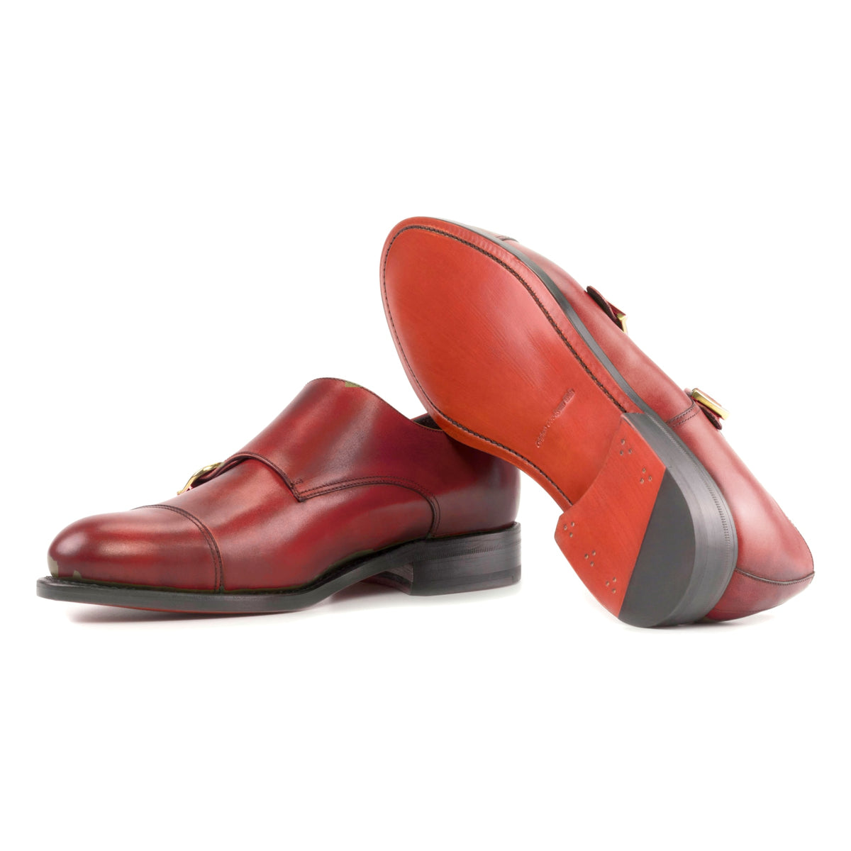 Chaussure double boucle en cuir teinté main rouge : une chaussure debout, l’autre couchée montre sa semelle