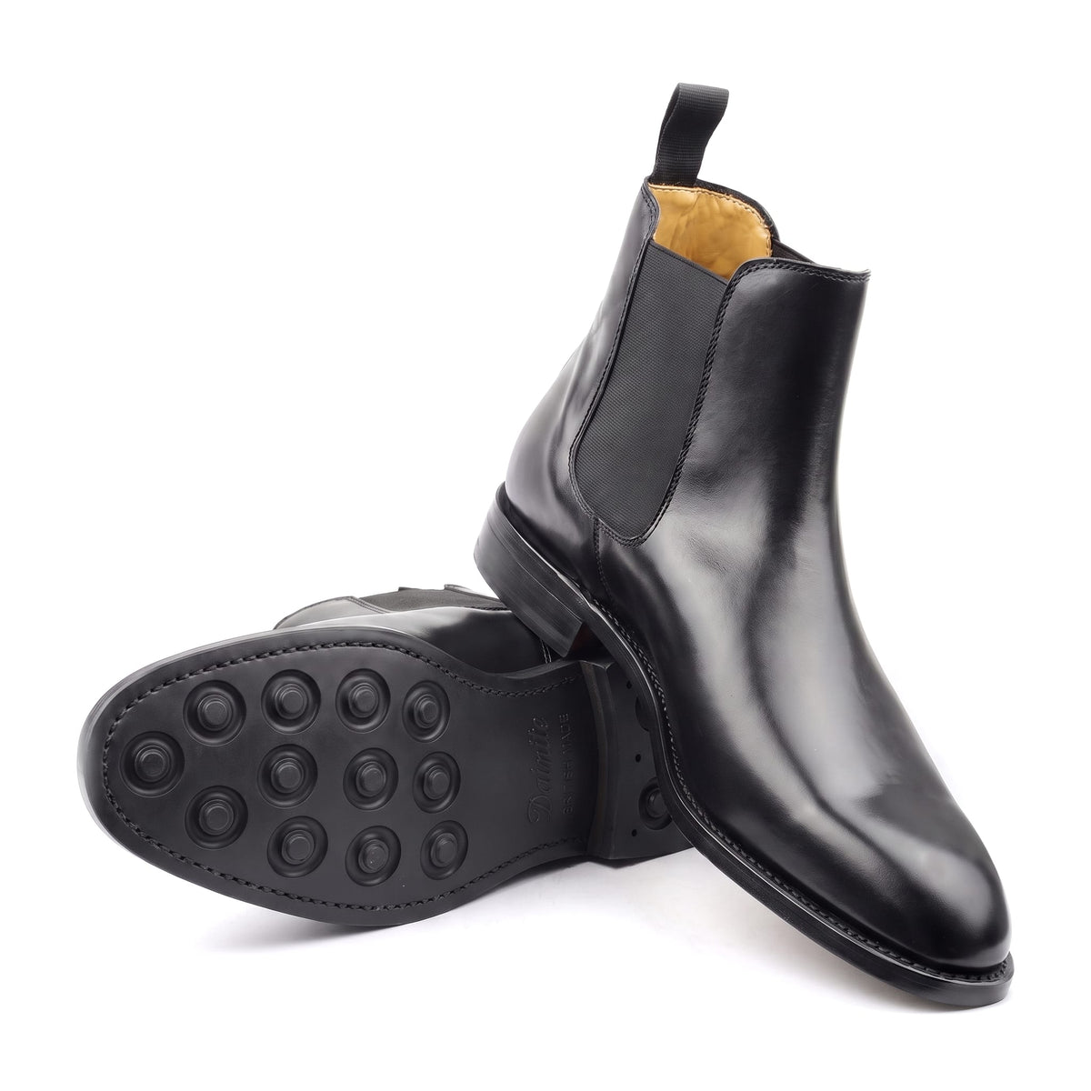 Chelsea boots en cuir noir : l’une debout, l’autre couchée pour montrer la semelle en caoutchouc Dainite à picots