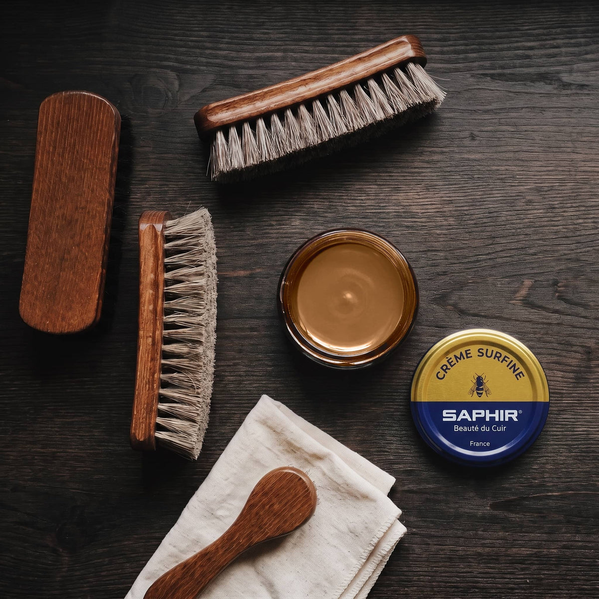 Crème Surfine Saphir Bronze en pot ouvert, avec des brosses en crin et une chamoisine, vue de dessus