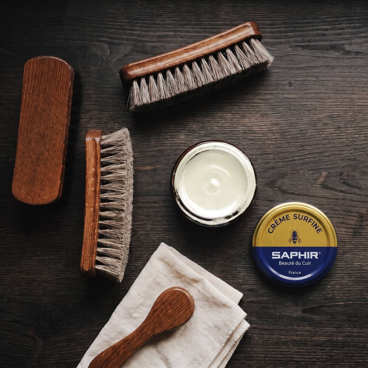 Crème Surfine Saphir Ivoire en pot ouvert, avec des brosses en crin et une chamoisine, vue de dessus