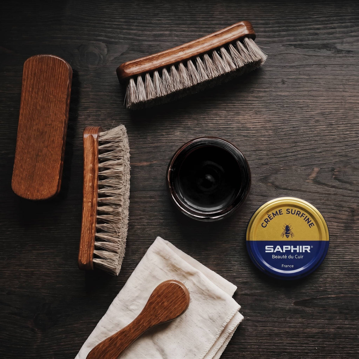 Crème Surfine Saphir Noir en pot ouvert, avec des brosses en crin et une chamoisine, vue de dessus