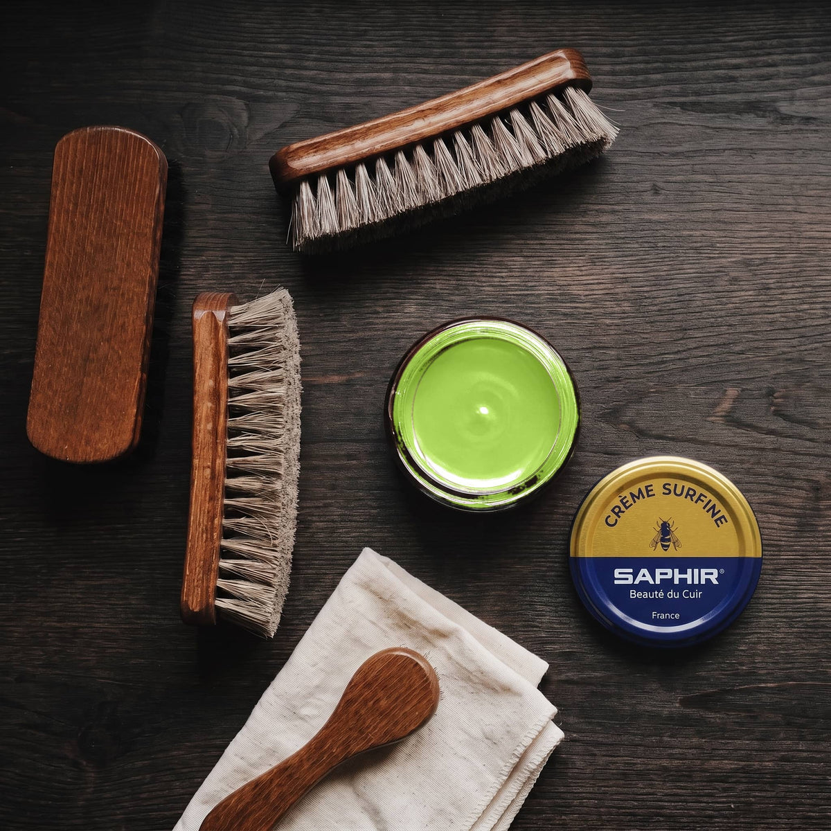 Crème Surfine Saphir Vert pomme en pot ouvert, avec des brosses en crin et une chamoisine, vue de dessus