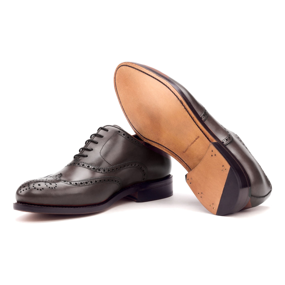 Richelieu fleuri en cuir teinté main marron foncé, semelle cuir : une chaussure debout, l’autre couchée montre sa semelle