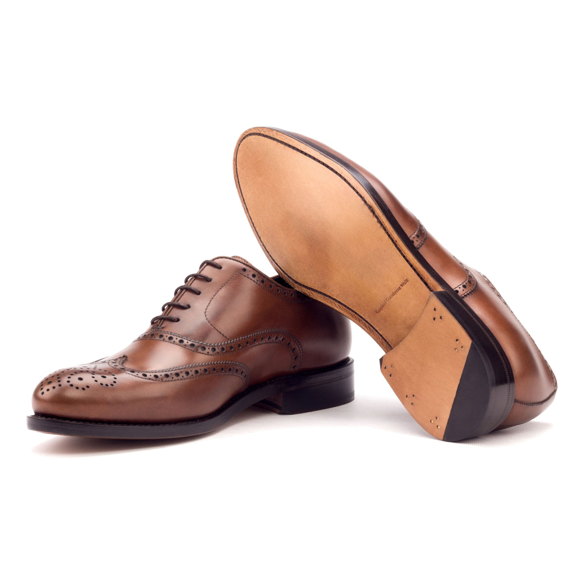 Richelieu fleuri en cuir teinté main marron moyen, semelle cuir : une chaussure debout, l’autre couchée montre sa semelle