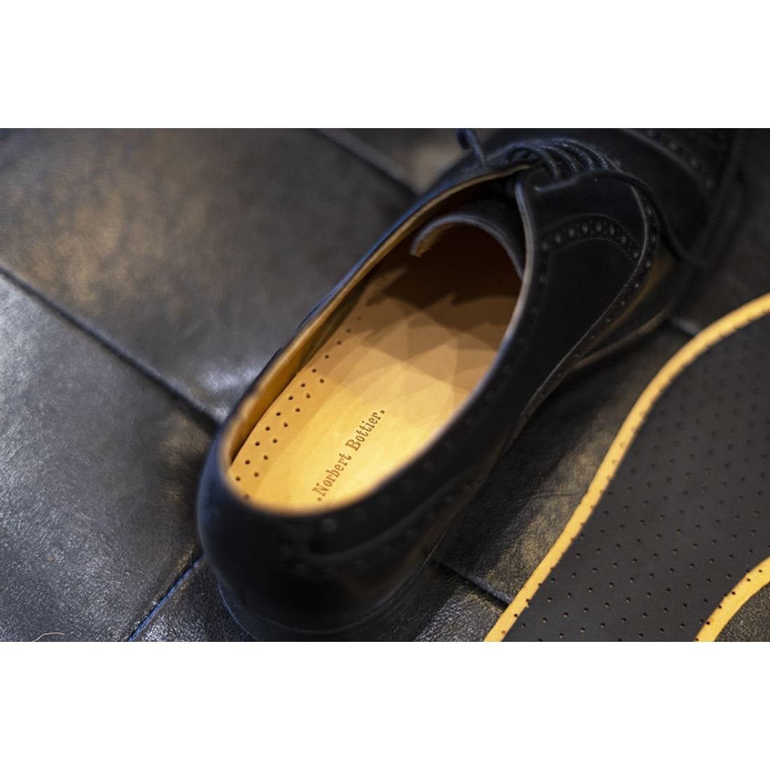 Semelle en cuir marquée Norbert Bottier, glissée dans un soulier noir à bout fleuri.