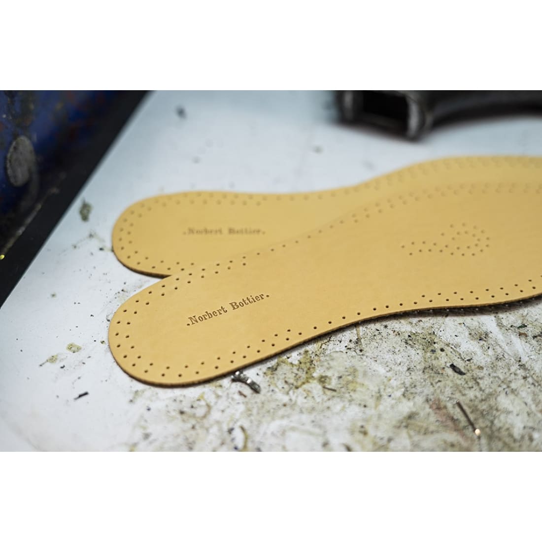 Deux semelles en cuir marquées Norbert Bottier sur l’établi de l’atelier.