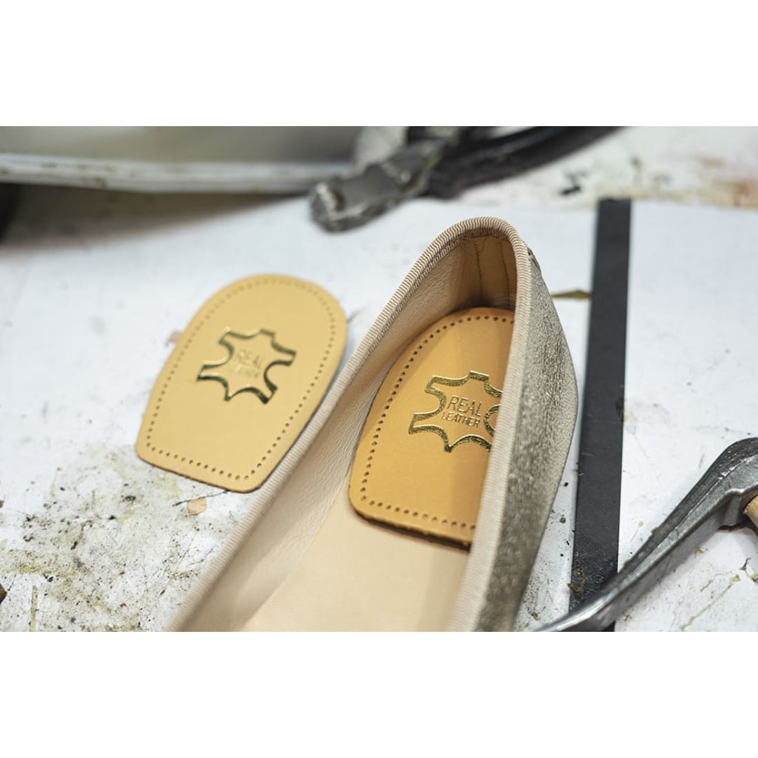 Talonnette en cuir posée au fond d’une chaussure plate beige, une seconde à côté.